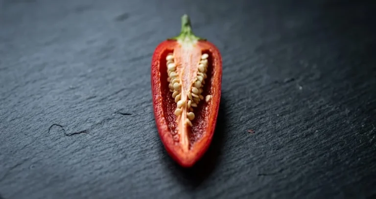 Cross-section of a halved red chili pod on dark slate showing the pale placenta and seeds