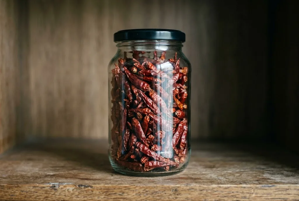 Ripe red Cili Padi peppers drying on a woven bamboo mat.